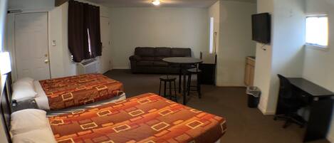 A hotel room with two beds, a sofa, a dining table, and a TV.