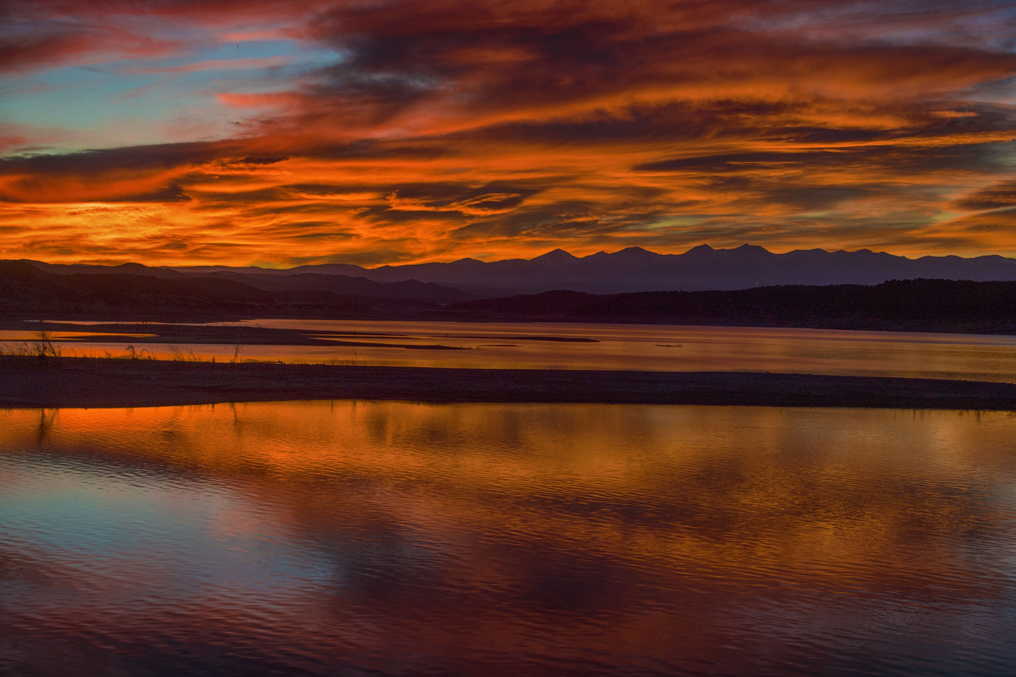 Een rustig meer dat een zonsondergang weerspiegelt, met bergen op de achtergrond.