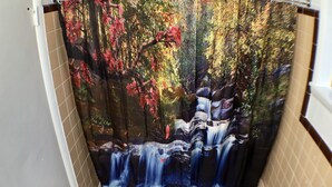 A bathroom with a shower curtain depicting a waterfall and autumn foliage. - Tower 64 Motel & RV Park (Trinidad)