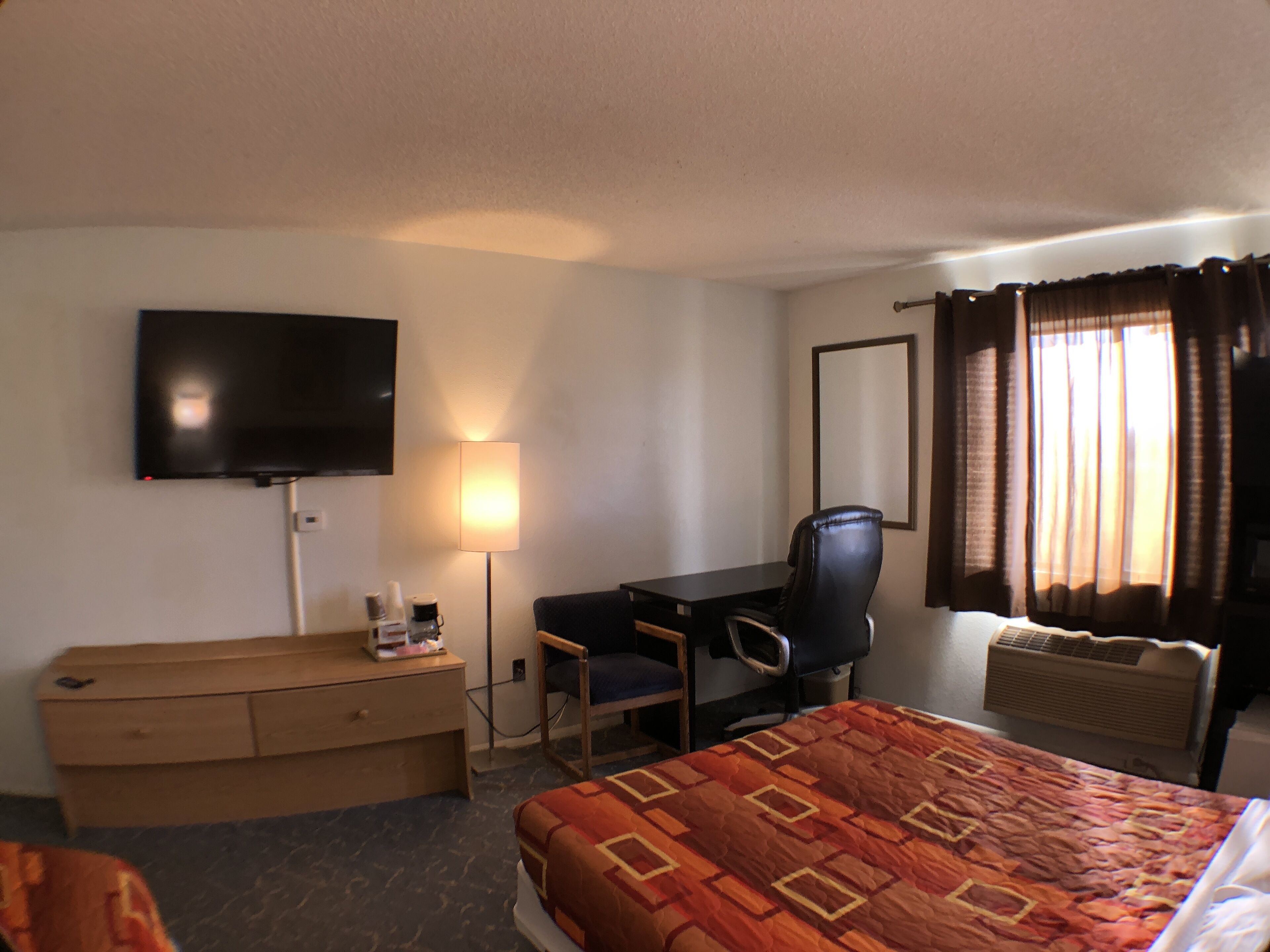 A hotel room with a bed, a desk, a chair, a television, a lamp, and a window with curtains.