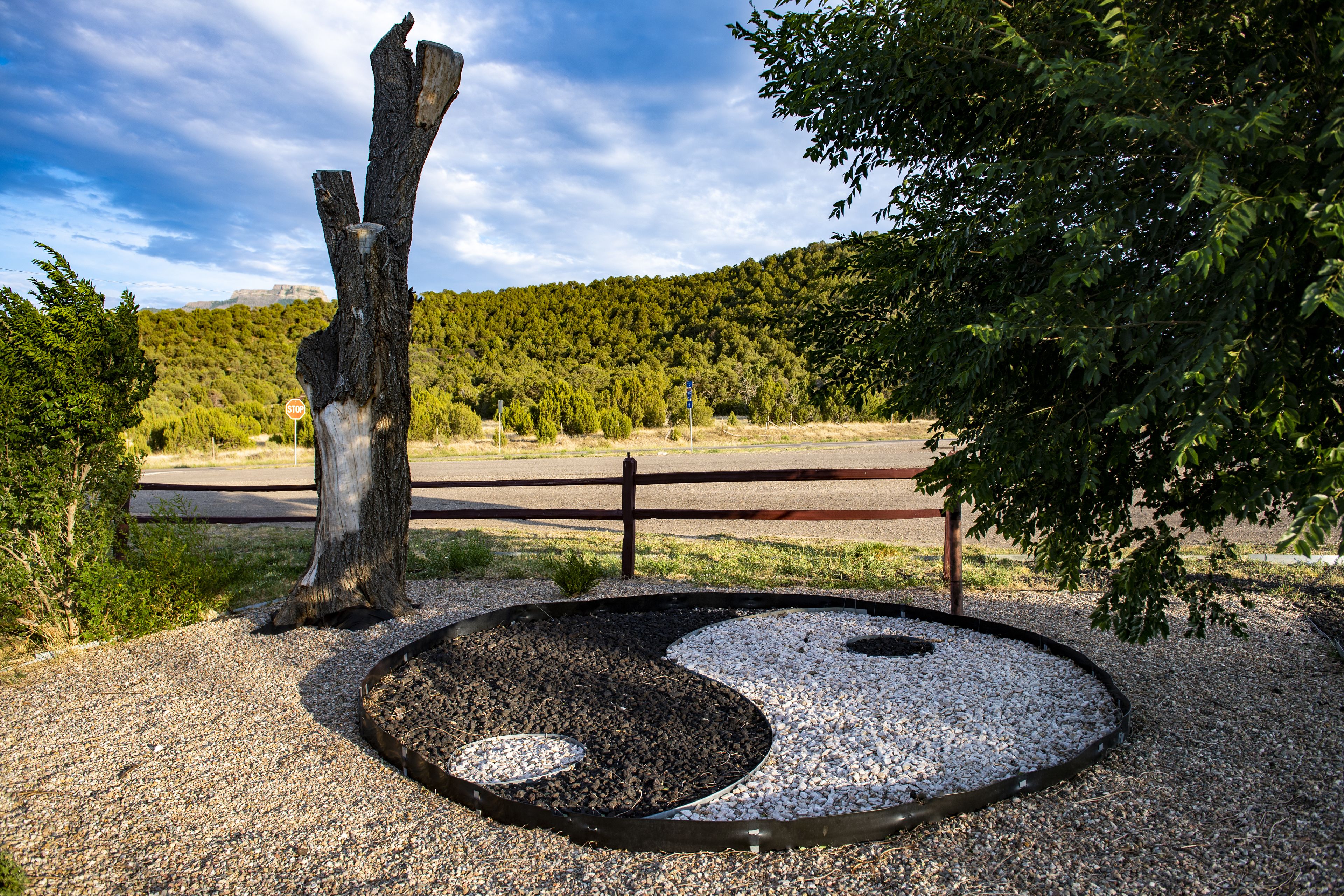 Un jardín zen con una roca grande, grava y una valla de madera.