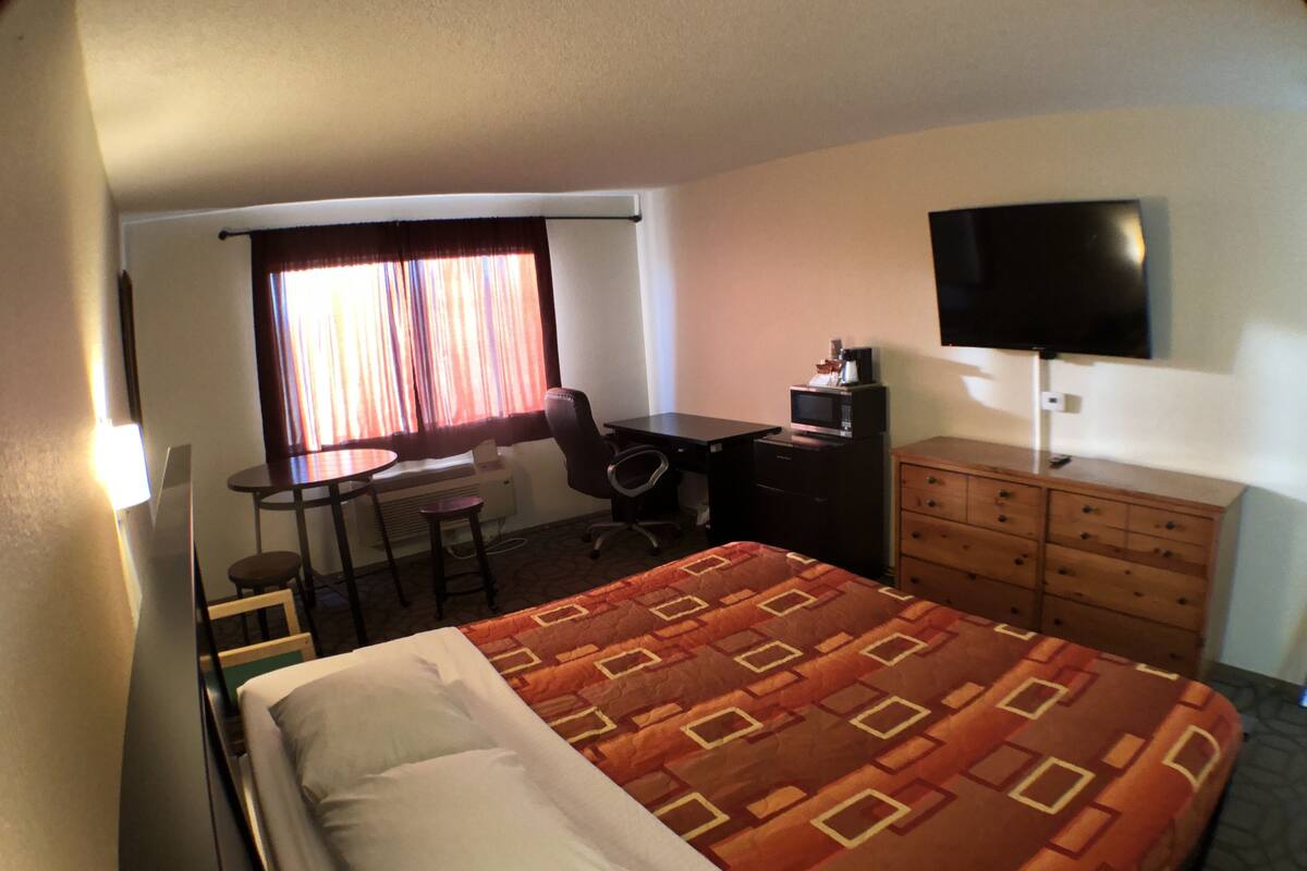 A hotel room with a bed, a desk with a chair, a television, and a dresser.