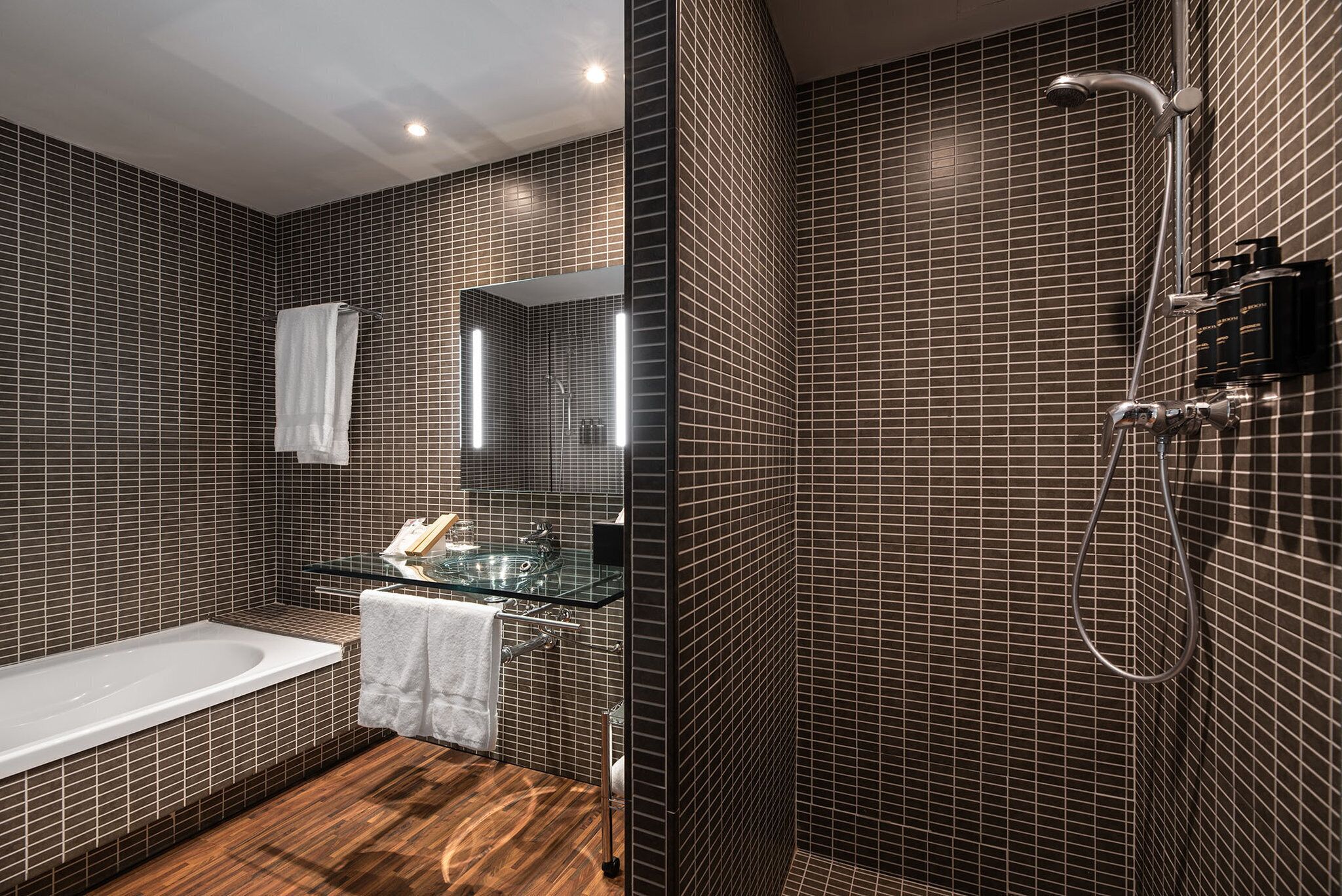 Un baño moderno con lavamanos de vidrio, una bañera y una zona de ducha.