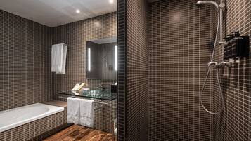 Un baño moderno con lavamanos de vidrio, una bañera y una zona de ducha.