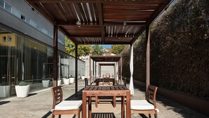 Eine Terrasse im Freien mit einer Holz-Pergola, einem Tisch mit Stühlen und Blumentöpfen.