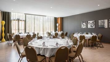A conference room with round tables, chairs, and a large window with curtains.
