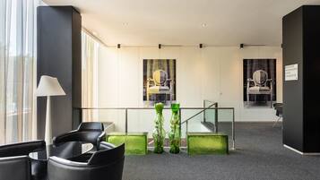 A modern lobby with black leather chairs, a glass table, green decorative vases, and a staircase with glass railings.