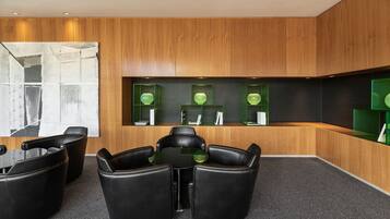 A modern conference room with black leather chairs around a glass table, wooden panel walls, and green shelving with decorative items.