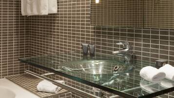 A modern bathroom with a glass sink, a bathtub, and a tiled wall.