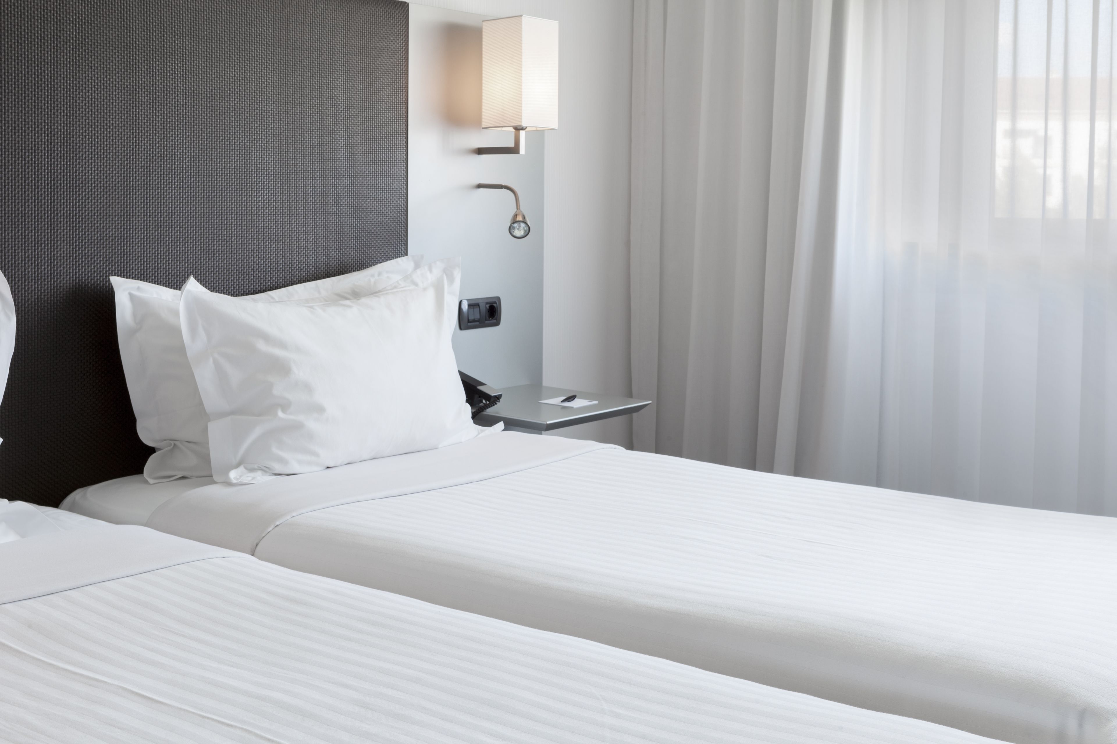 A hotel room with two beds, a bedside table, a lamp, and a window with curtains.