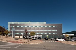 Een modern gebouw met een plat dak, meerdere ramen en een parkeerplaats met verschillende auto's.