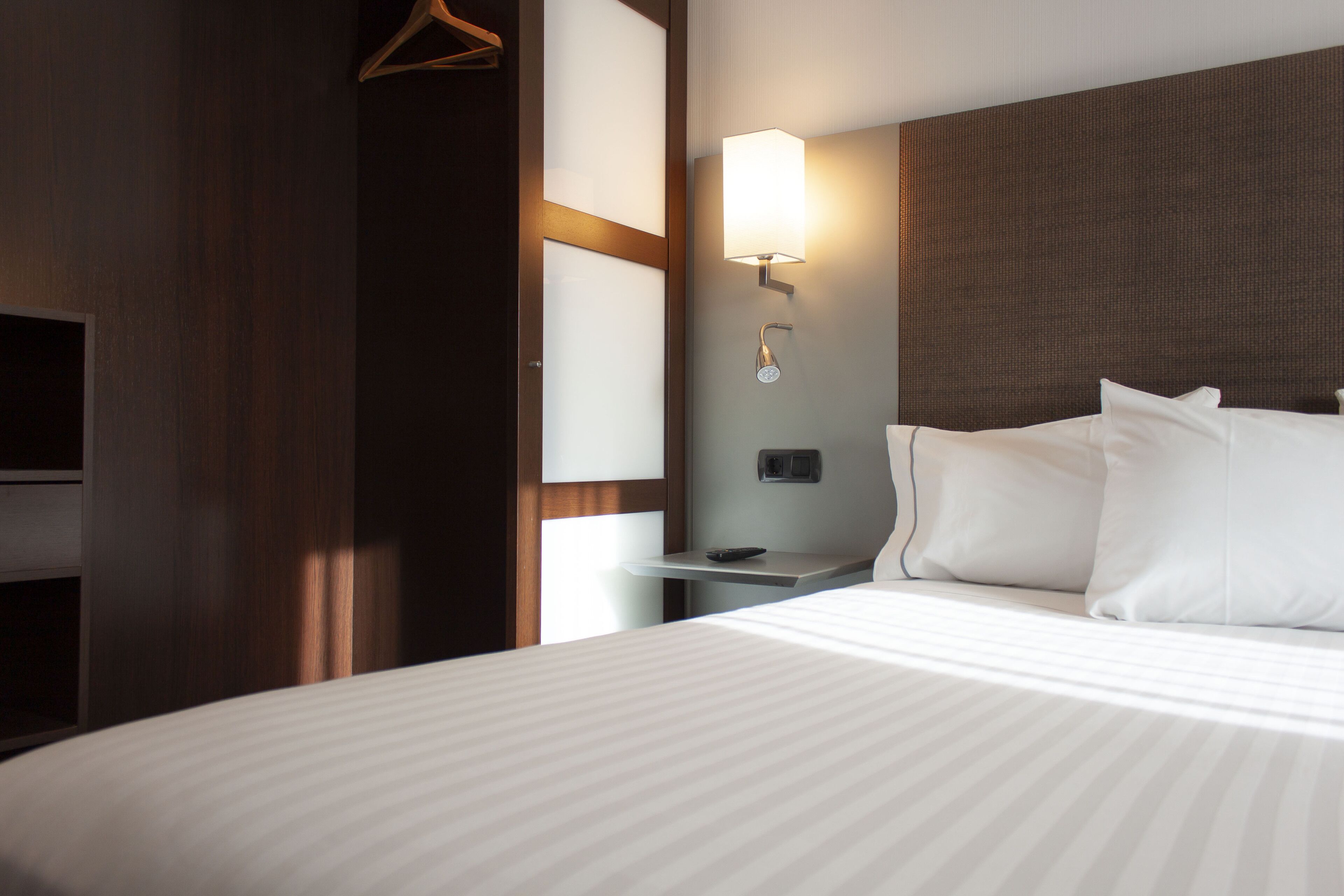 A hotel room with a large bed, a bedside table, a wall-mounted lamp, and a television.