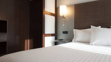 A hotel room with a large bed, a bedside table, a wall-mounted lamp, and a television.