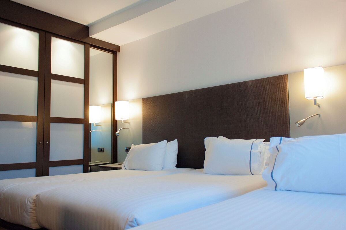 Ein Hotelzimmer mit zwei Betten, einem großen Spiegel und Wandleuchten.
