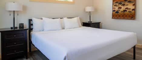 A neatly made bed with white linens, two bedside tables with lamps, a window with a wooden frame, and a patterned tapestry on the wall.