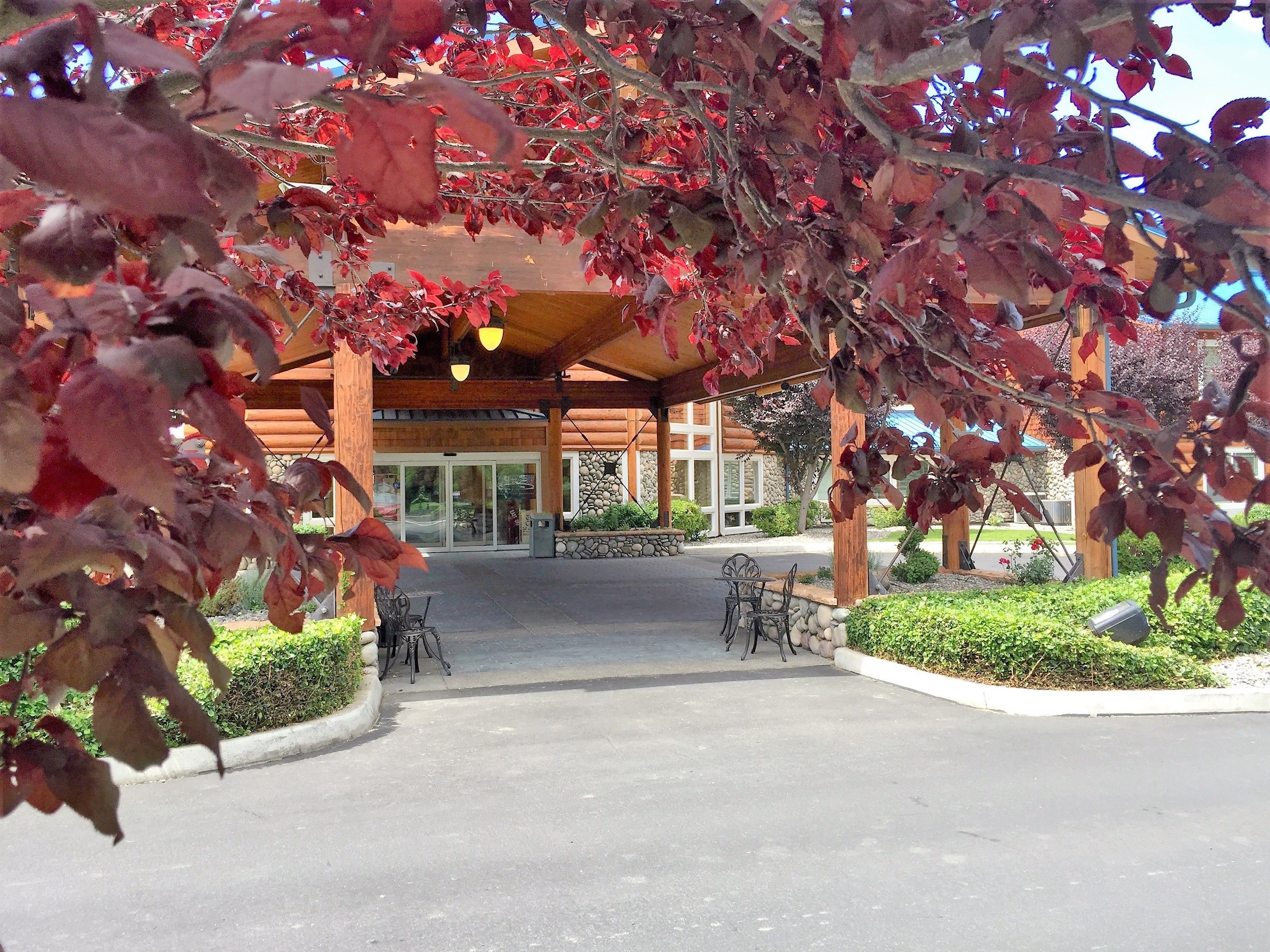 A covered outdoor area with a building entrance, outdoor seating, and a stone wall.
