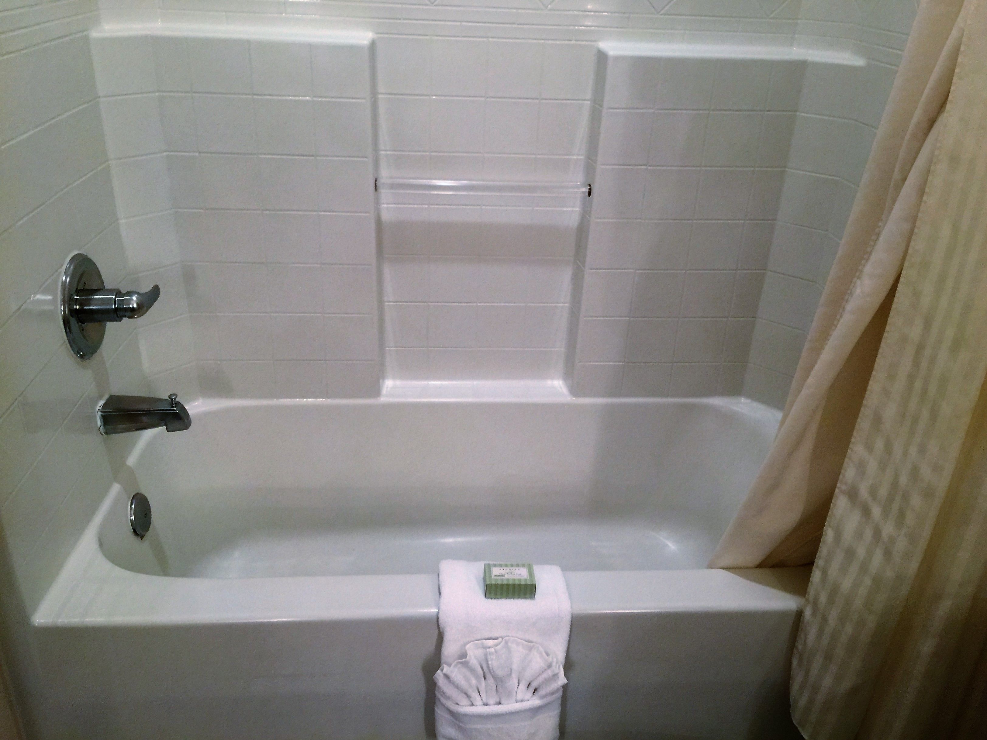 Una bañera blanca estándar con cortina de ducha, un perchero y un cubo de basura.