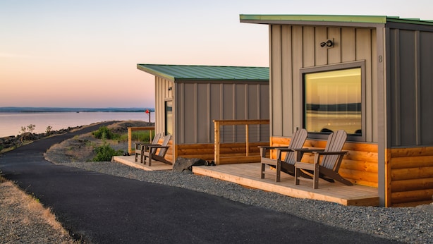 A cabin with a porch, two Adirondack chairs, and a view of the water. - River Lodge and Cabins (Boardman)