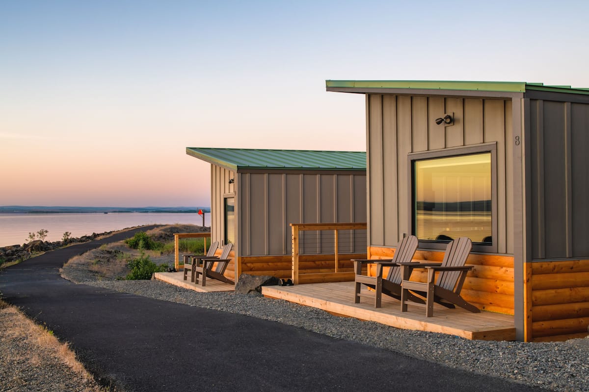 A cabin with a porch, two Adirondack chairs, and a view of the water.