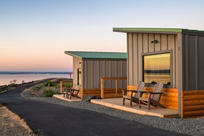 A cabin with a porch, two Adirondack chairs, and a view of the water. - River Lodge and Cabins (Boardman)