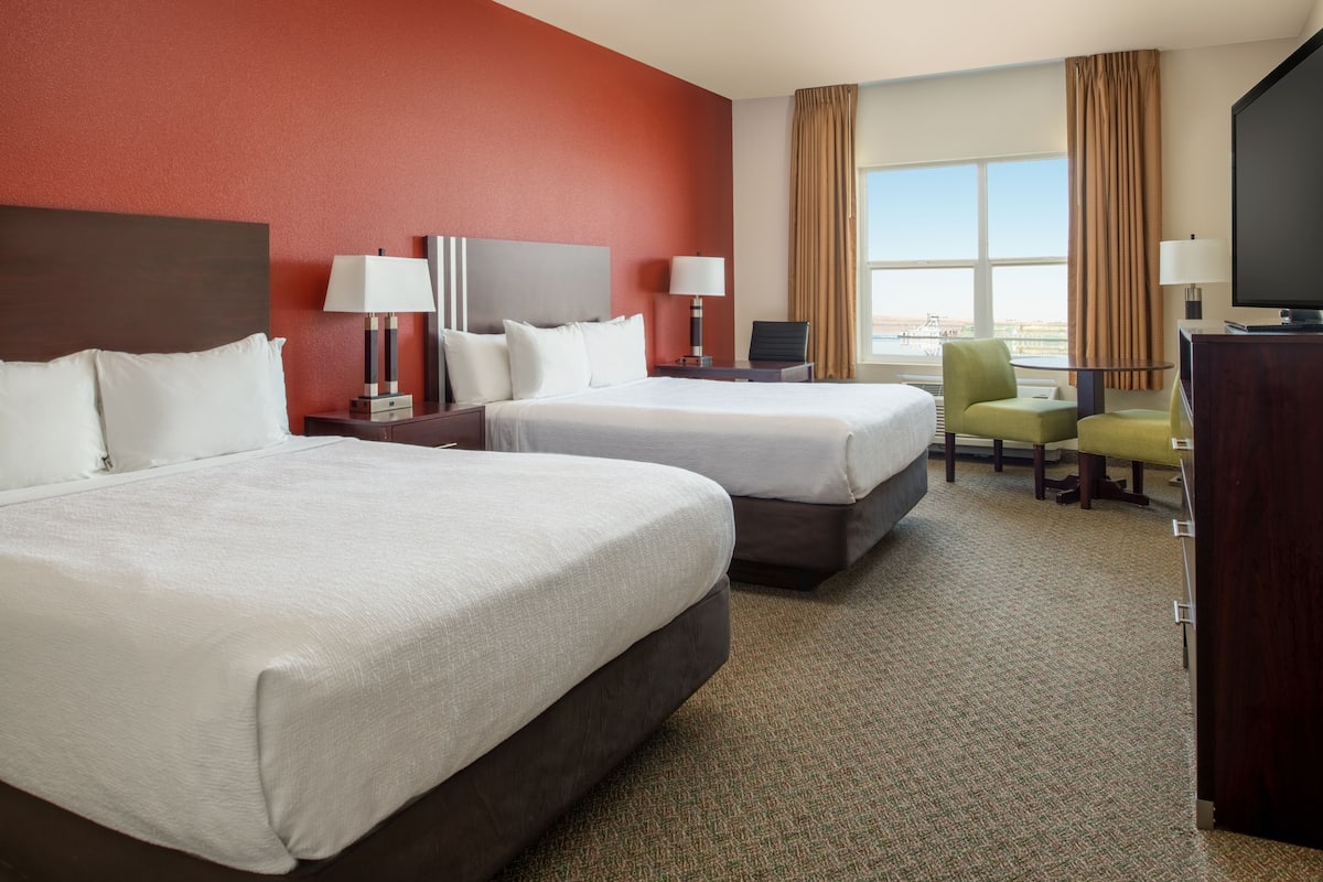A hotel room with two beds, a desk, a chair, a television, and a view of the city.