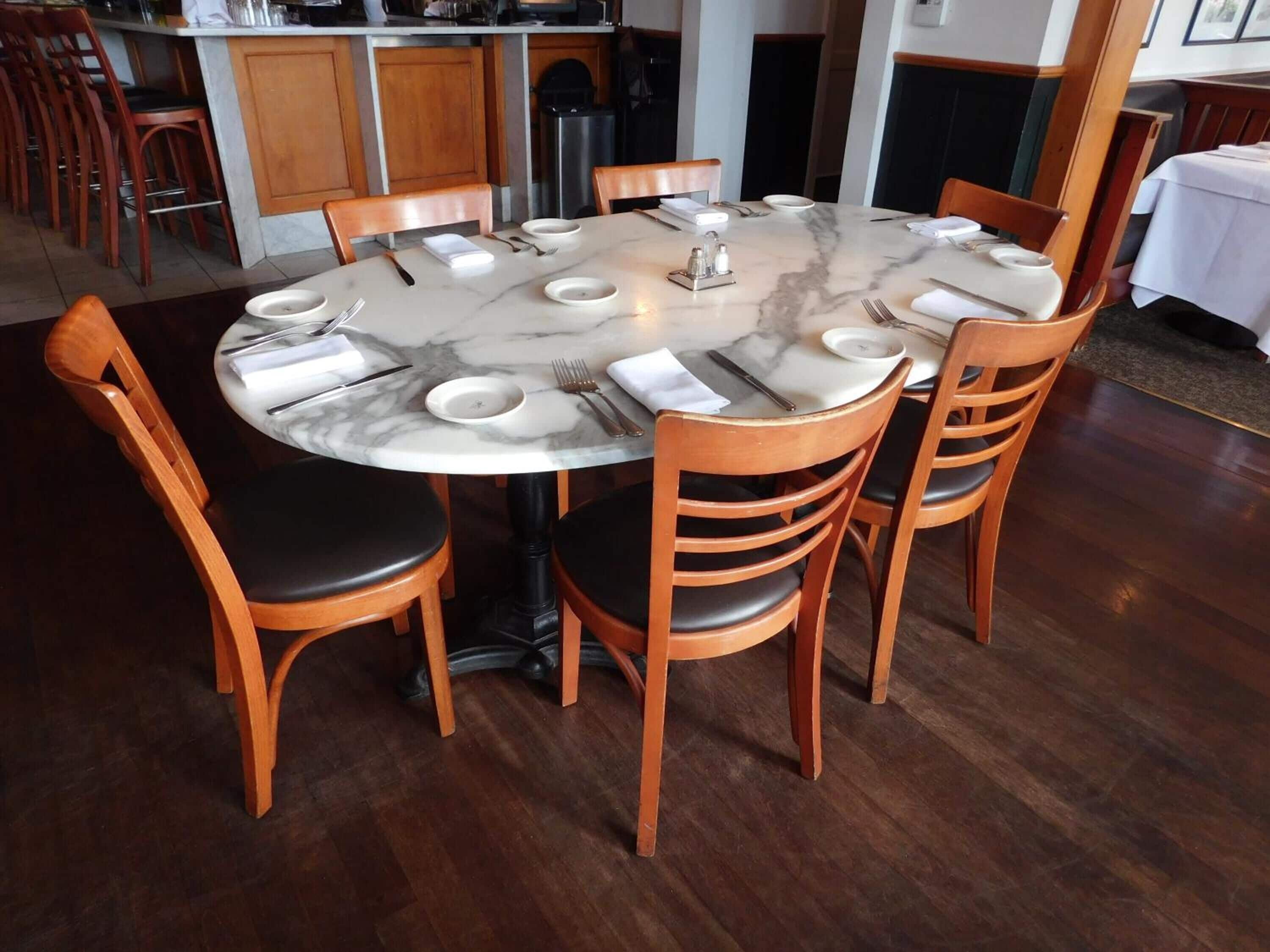 Una mesa redonda de comedor con seis sillas de madera, una superficie de mármol y un mantel blanco.