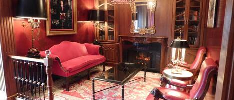 A traditional room with a red sofa, a fireplace, a chandelier, and a bookshelf.