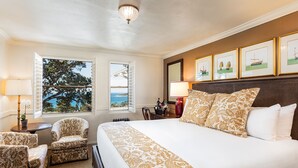 Une chambre d’hôtel avec un grand lit, deux fauteuils, une petite table et une fenêtre donnant sur l’océan.
