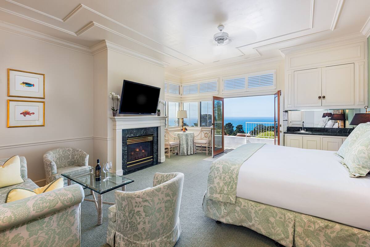 Una camera d'albergo con camino, televisione, un balcone vista mare e angolo cottura.