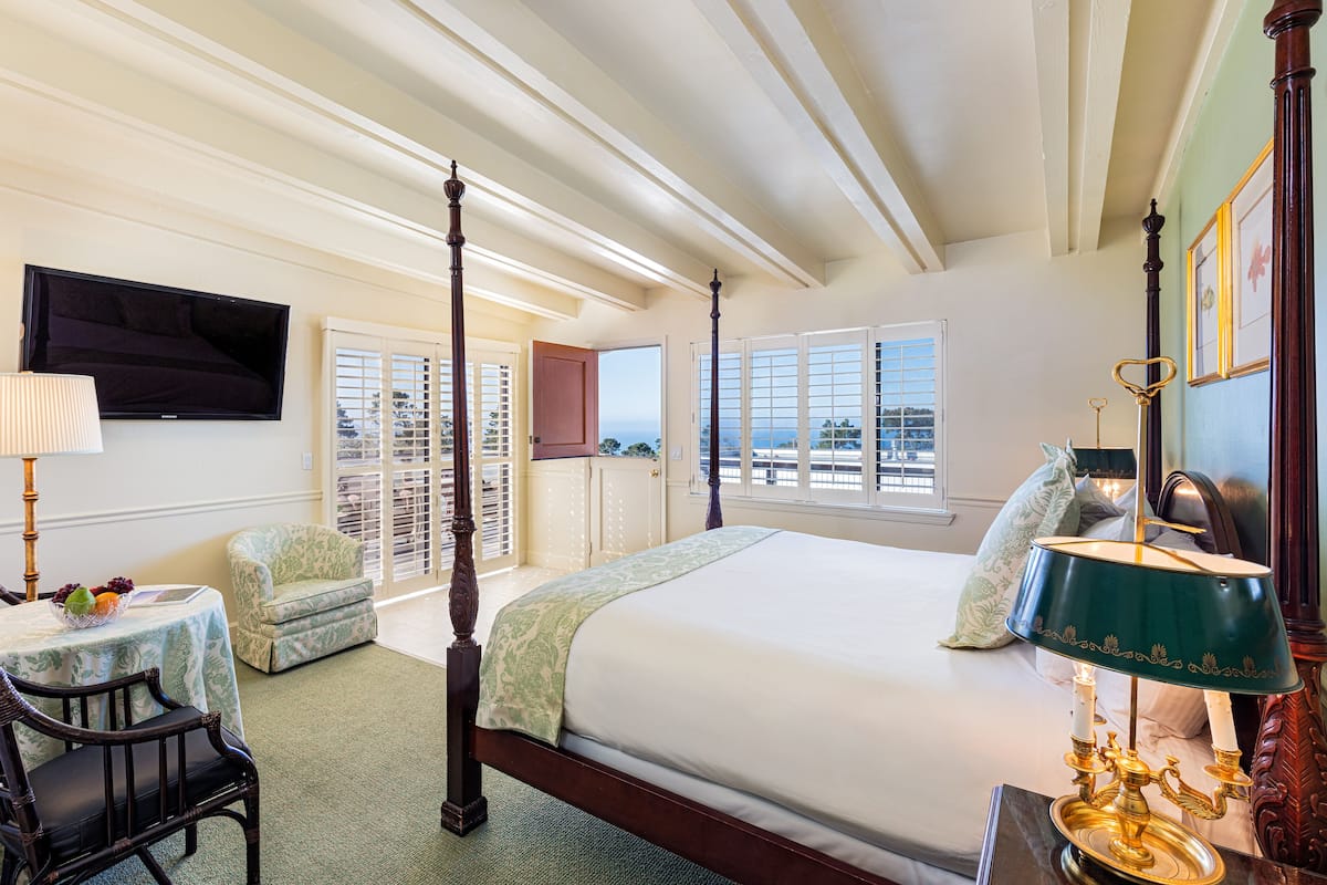 Un'ampia camera da letto con un letto a baldacchino, una televisione a parete, un tavolino con una lampada e vista sull'oceano attraverso ampie finestre.