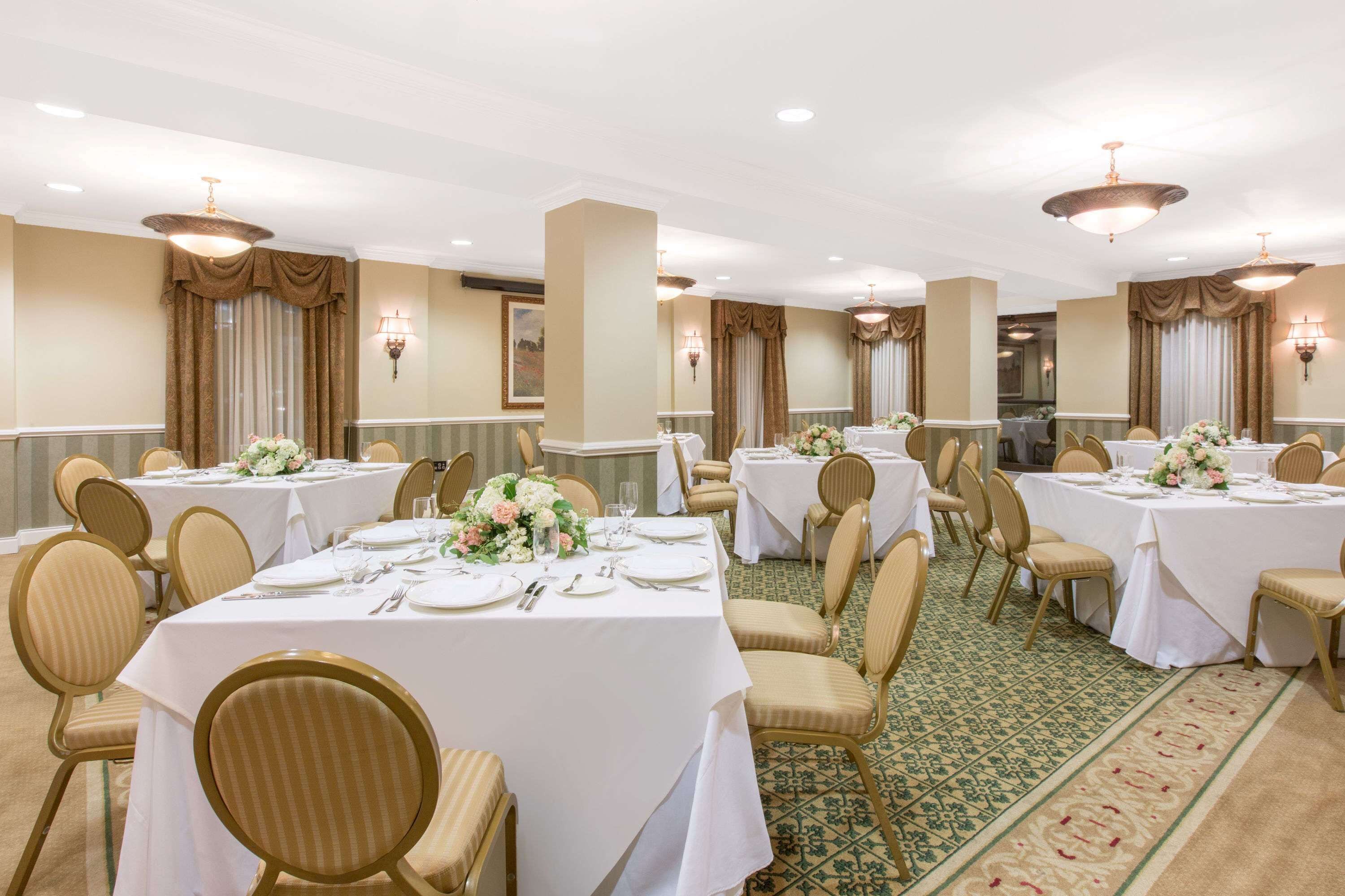 A banquet hall with multiple round tables, each set with white tablecloths, gold chairs, and floral centerpieces.