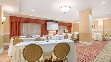 A conference room with multiple tables, chairs, and a large screen.