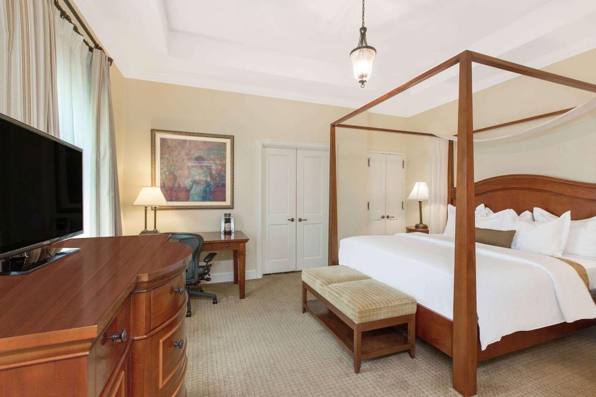 A four-poster bed, a television, a desk with a chair, and a painting on the wall.