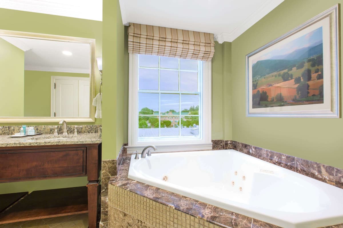A bathroom with a large bathtub, a window with a view, and a painting on the wall.