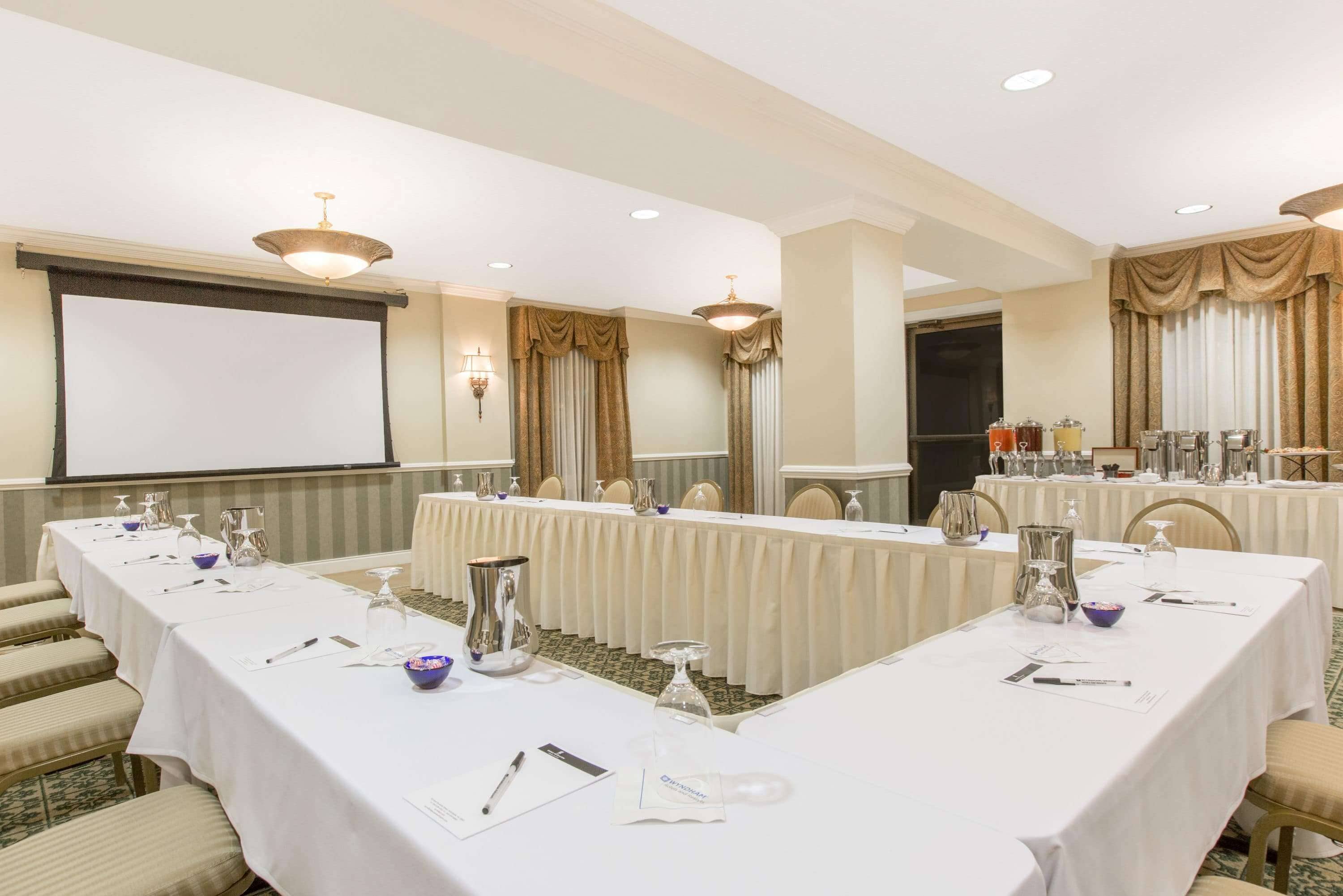 Una sala conferenze con un lungo tavolo, sedie, uno schermo per proiettore e un'area buffet.