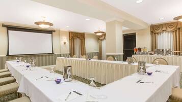 Una sala conferenze con un lungo tavolo, sedie, uno schermo per proiettore e un'area buffet.