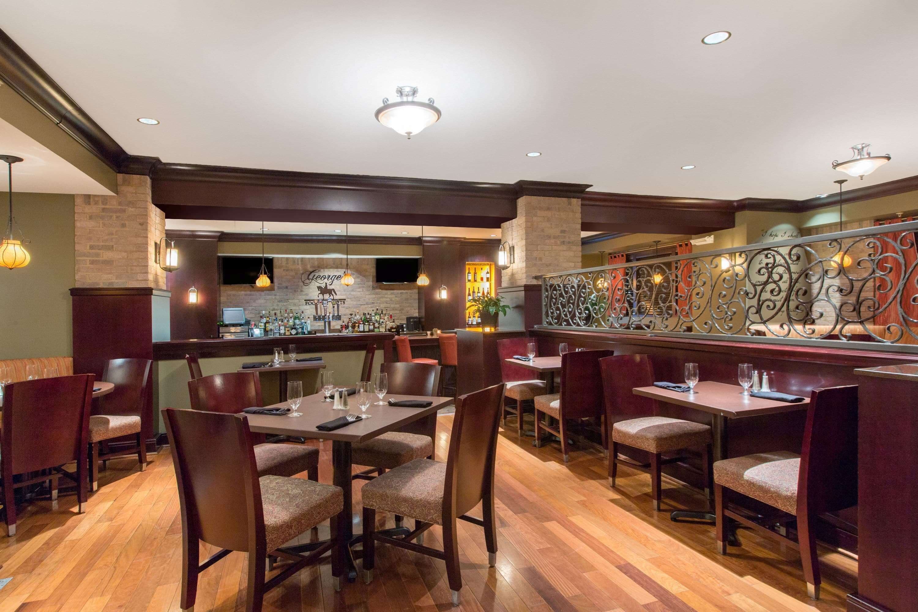 A restaurant with wooden flooring, multiple tables and chairs, a bar area, and decorative wall sconces.