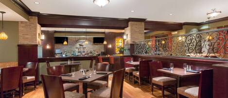 Un restaurante con suelo de madera, varias mesas y sillas, una zona de bar y apliques decorativos en la pared.