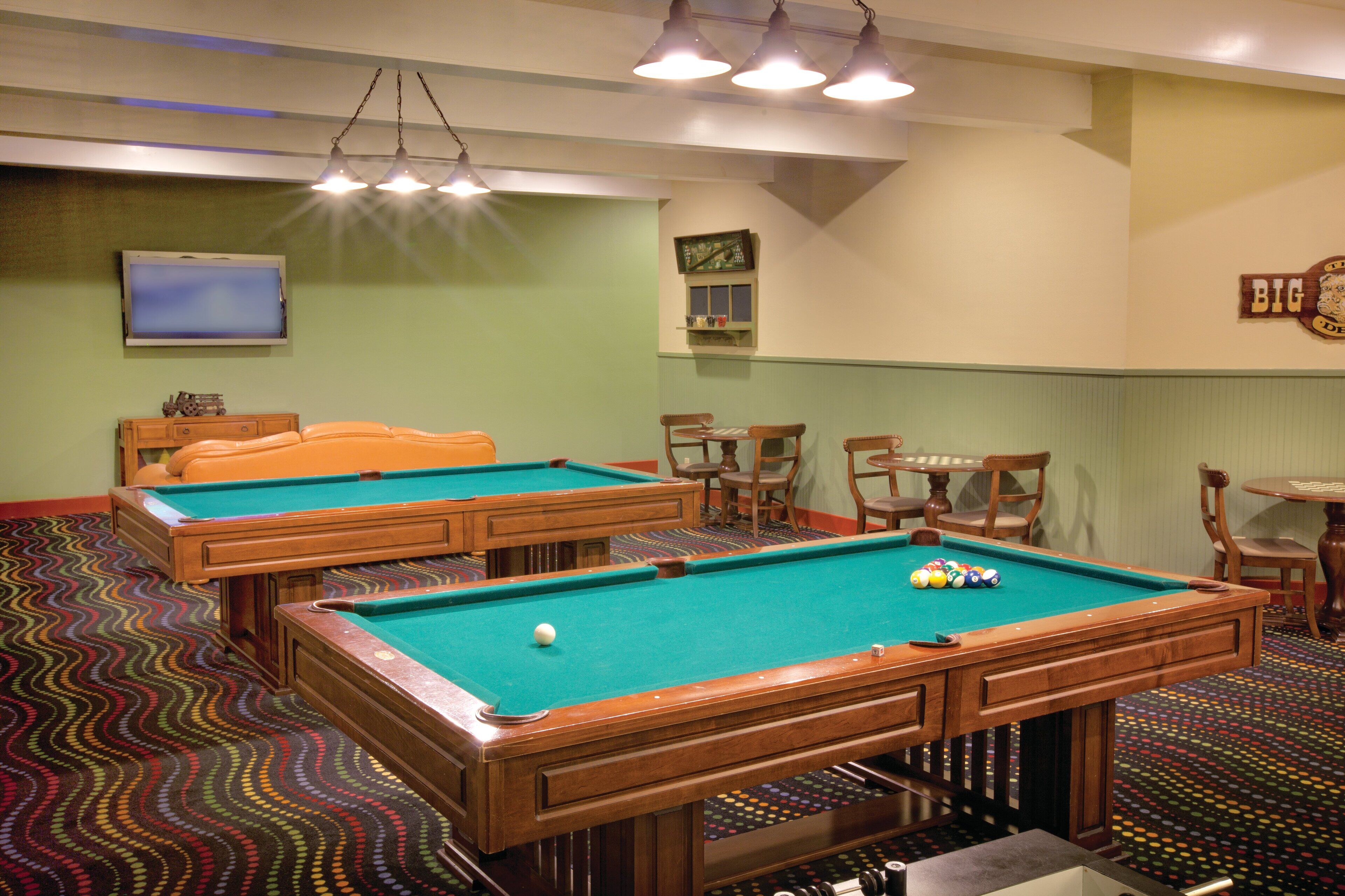 A pool table with a ball, a television, and a clock on the wall.
