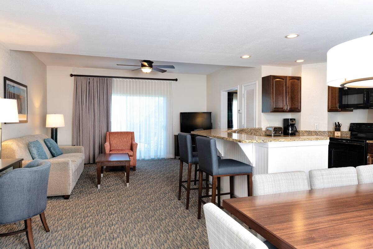 Habitación de hotel con sala de estar, mesa de comedor, cocina con microondas y ventilador de techo.