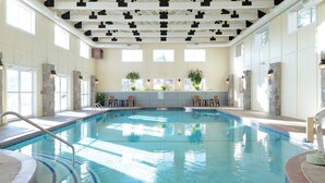 An indoor swimming pool with clear water, stone pillars, and a ceiling with geometric patterns.