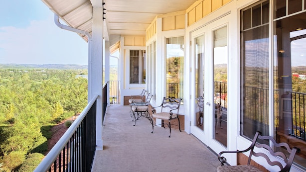 A covered balcony with a view of a forested landscape, featuring a table and two chairs.
