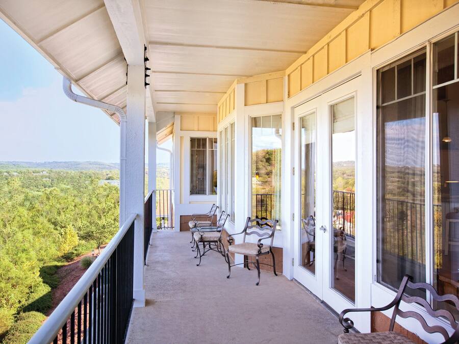 A covered balcony with a view of a forested landscape, featuring a table and two chairs.
