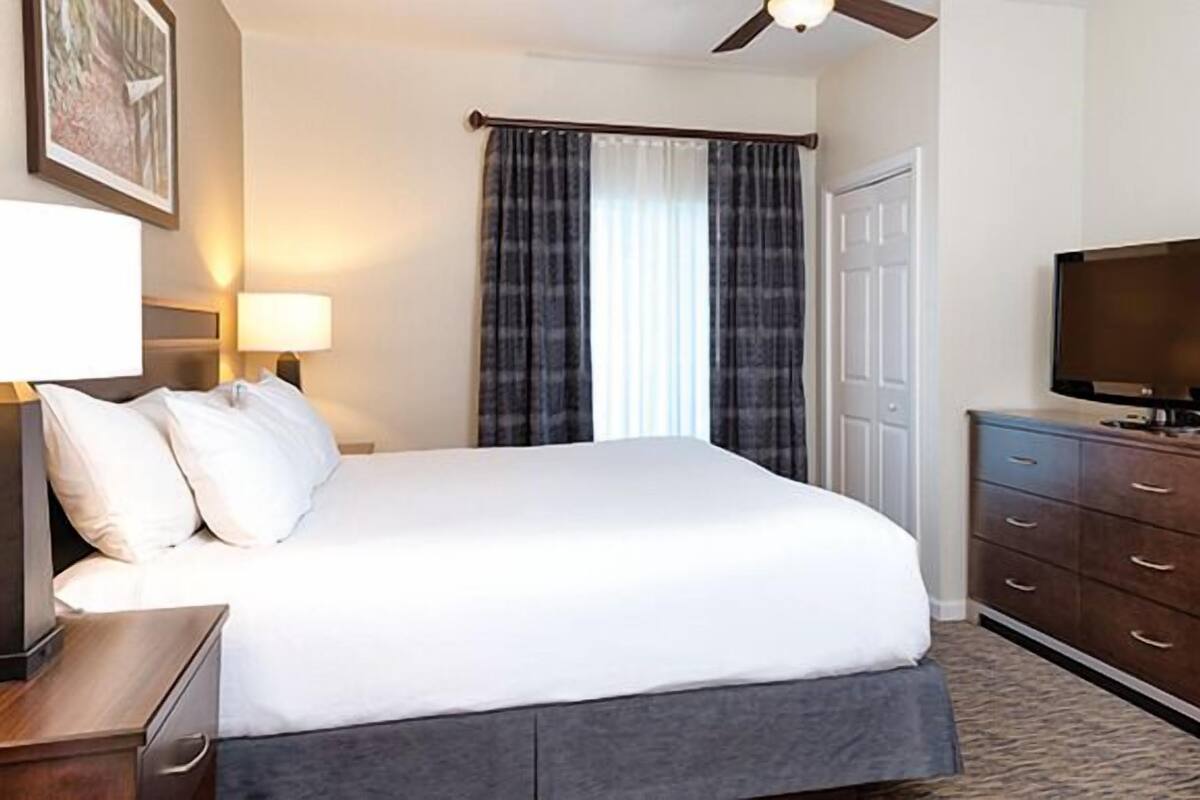 Una habitación de hotel con una cama grande, un televisor en una cómoda y una ventana con cortinas.