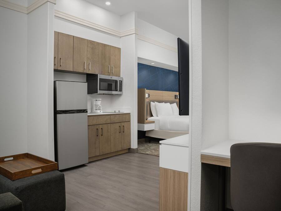 Une chambre d’hôtel de taille réduite, équipée d’une kitchenette, d’un lit, d’un bureau et d’une chaise.