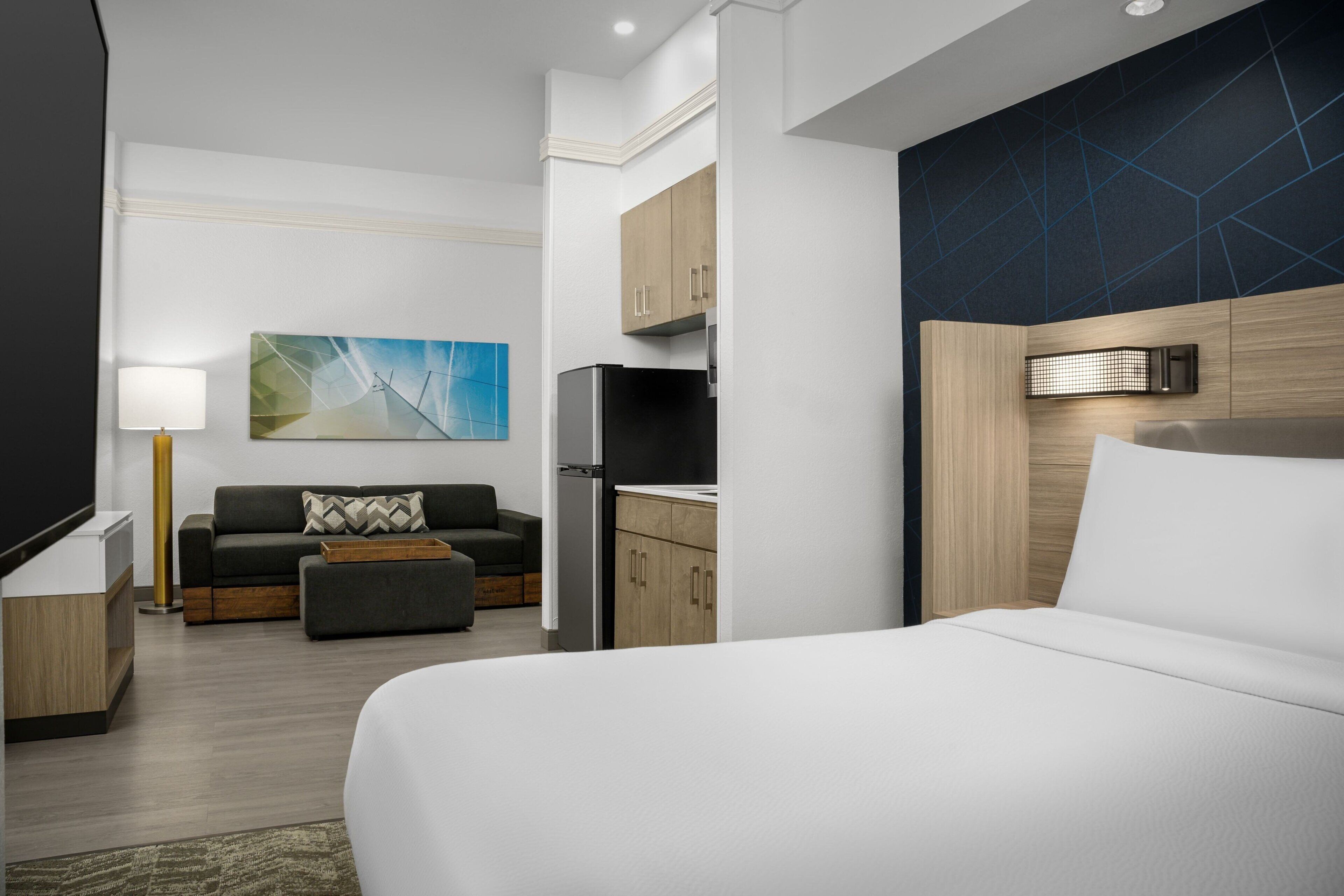 Una habitación de hotel moderna con una cama grande, un sofá, una pequeña cocina y un televisor de pantalla plana.