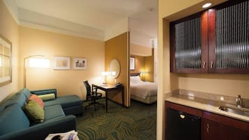 A hotel room with a sofa, a desk, a bed, and a kitchenette.