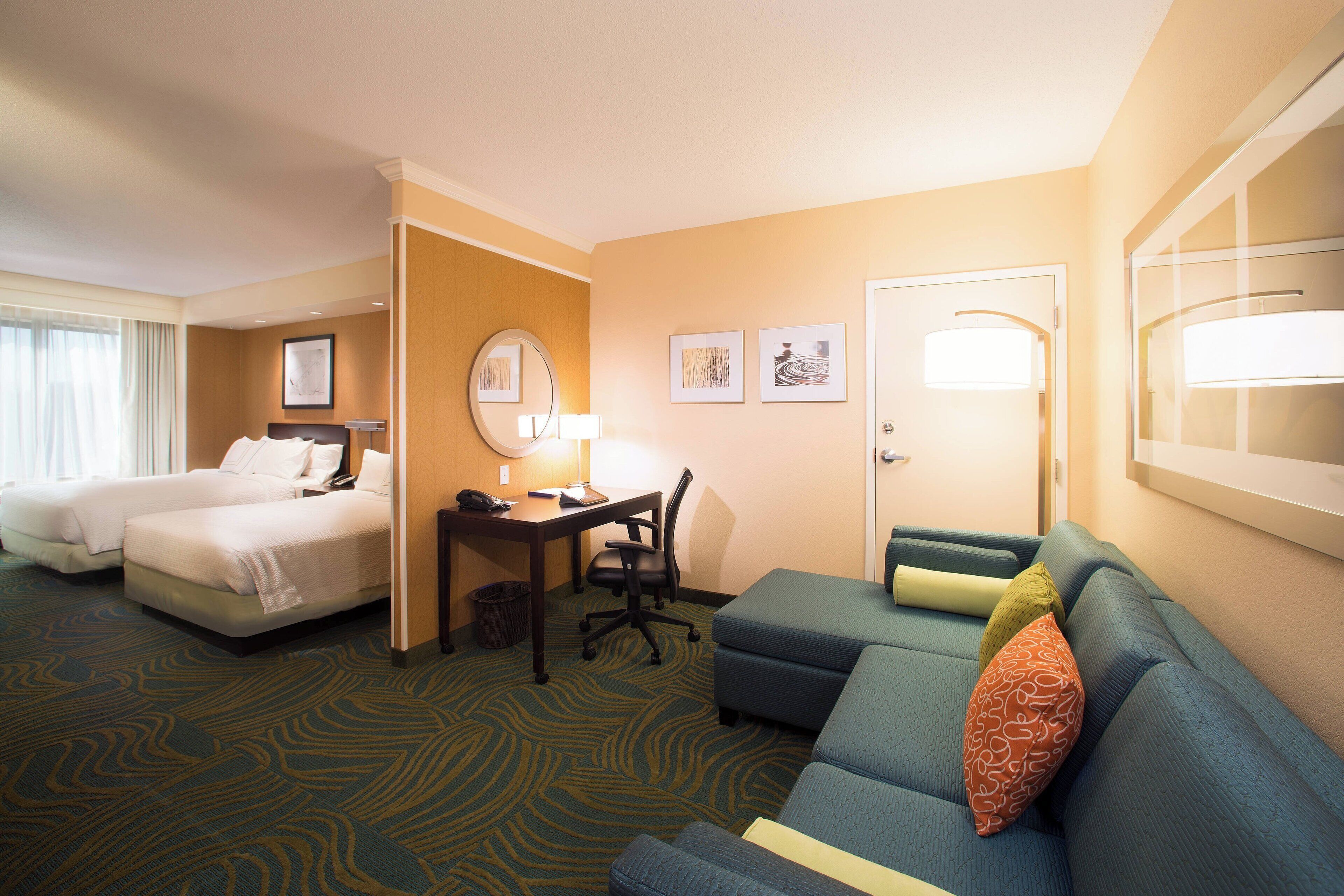 A hotel room with two beds, a desk, a chair, a sofa, and a large mirror.