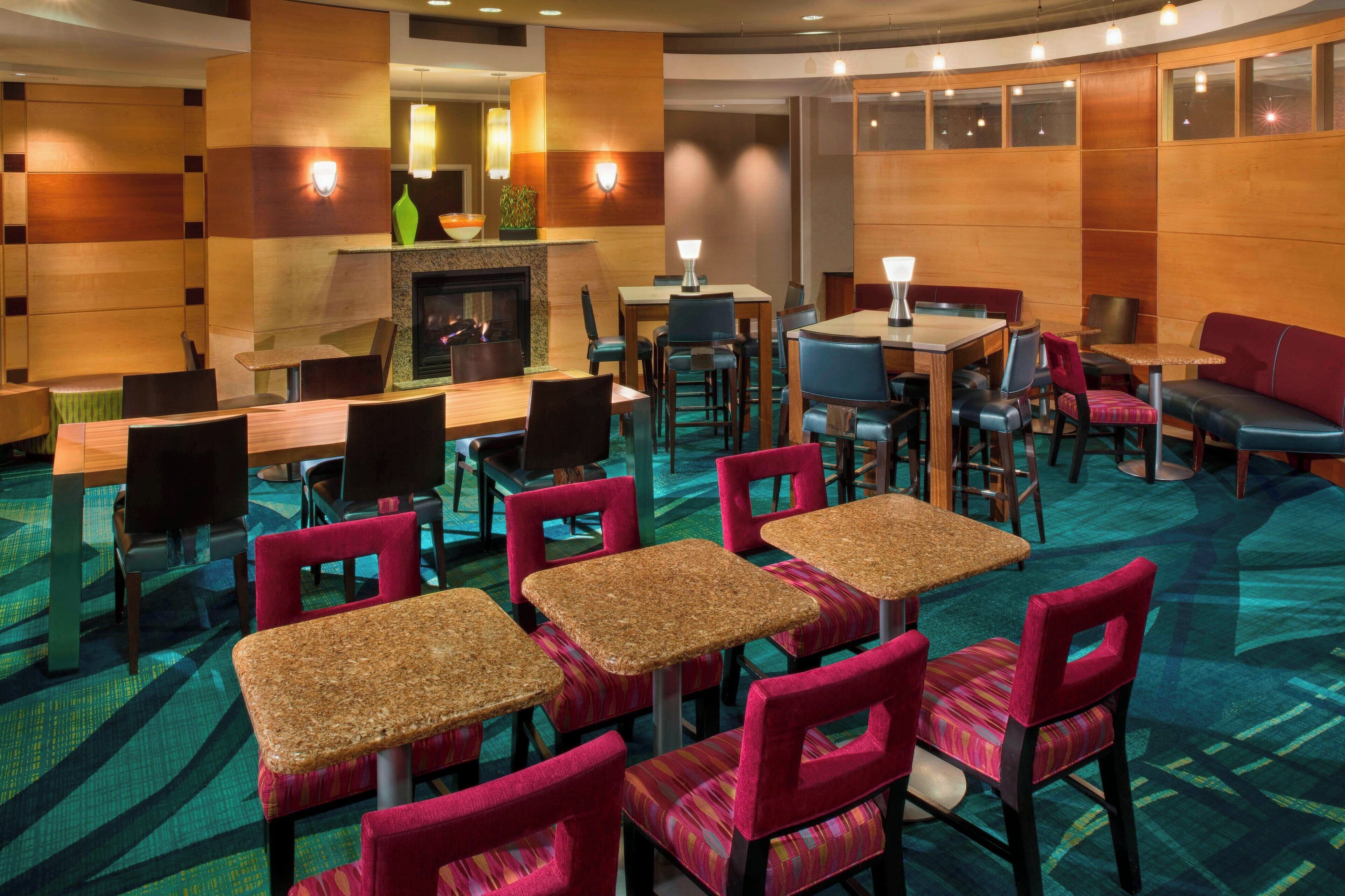 A hotel lobby with multiple seating areas, including tables and chairs, a fireplace, and a bar area.