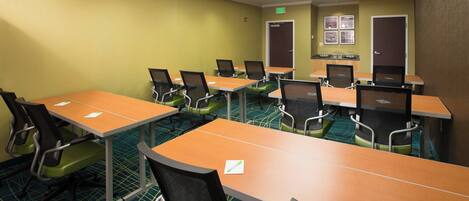 A conference room with multiple tables and chairs, a carpeted floor, and a door with a sign.
